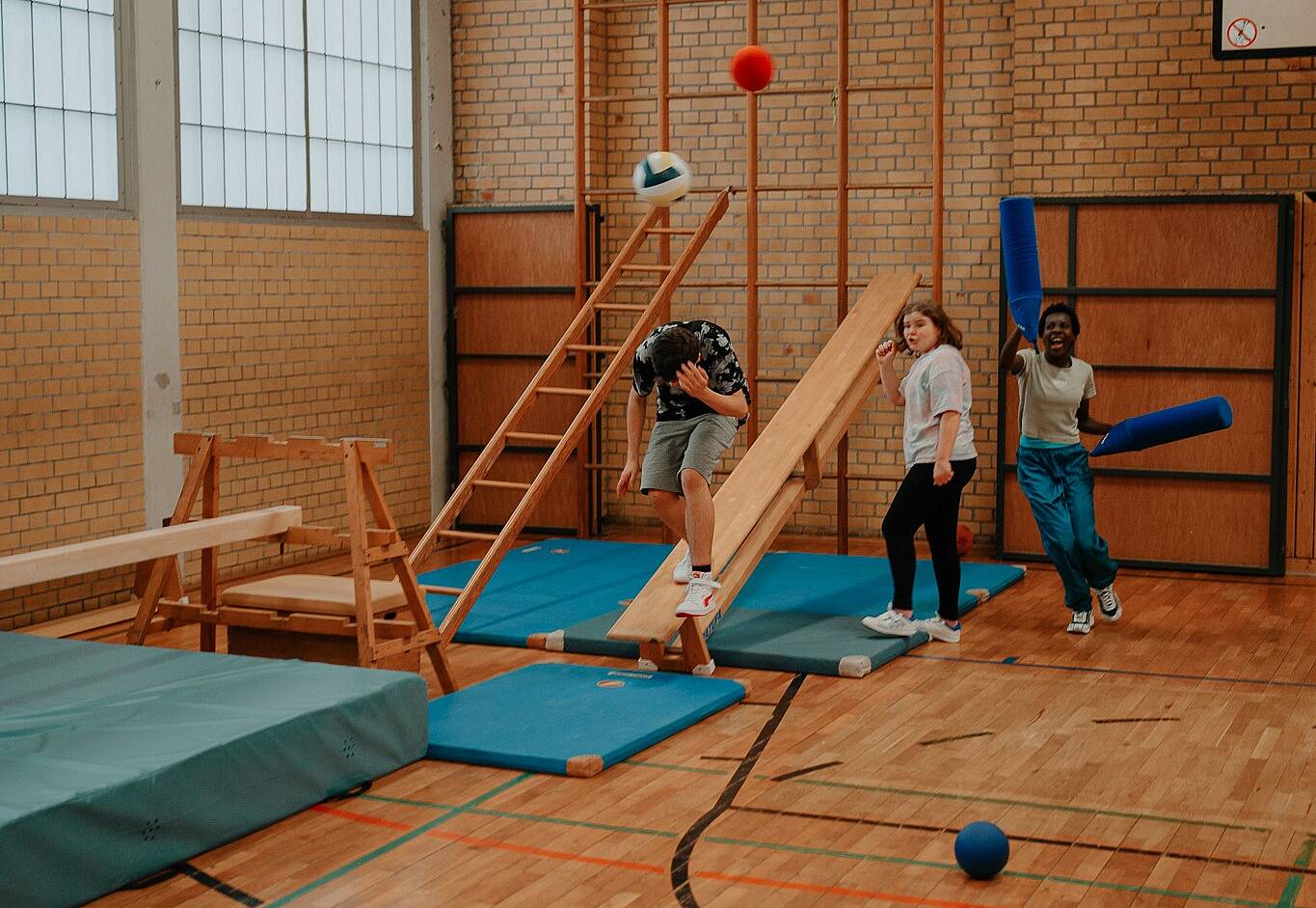 Kinder in einer Turnhalle klettern. Bälle fliegen durch die Luft.